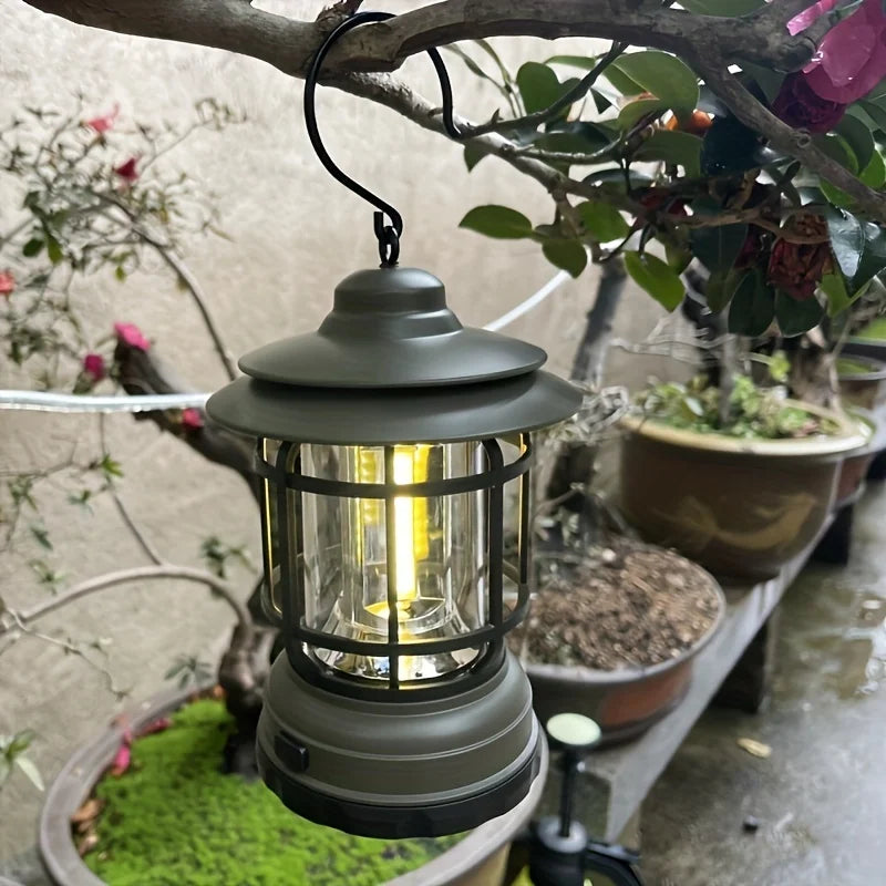 Rechargeable retro camping light in green hanging from a tree, providing LED illumination for outdoor adventures and garden use.