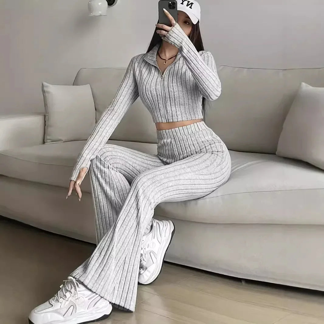 Gray striped 2-piece women's outfit with ribbed crop top and flared pants, styled with a cap and sneakers for a sporty lounge look.