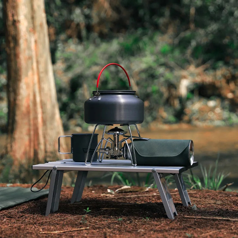 Folding Camping Table - Ultralight Travel Desk with kettle and thermos by riverside. Durable aluminum design for outdoor cooking.
