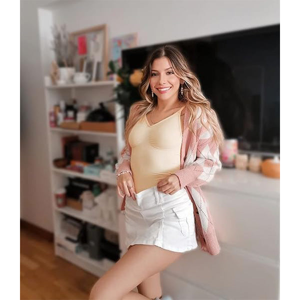 Woman wearing nude seamless tummy control bodysuit styled with white mini skirt and pink cardigan for a casual chic look.